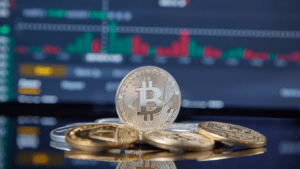 Bitcoin and gold coins on a table with a stock market screen