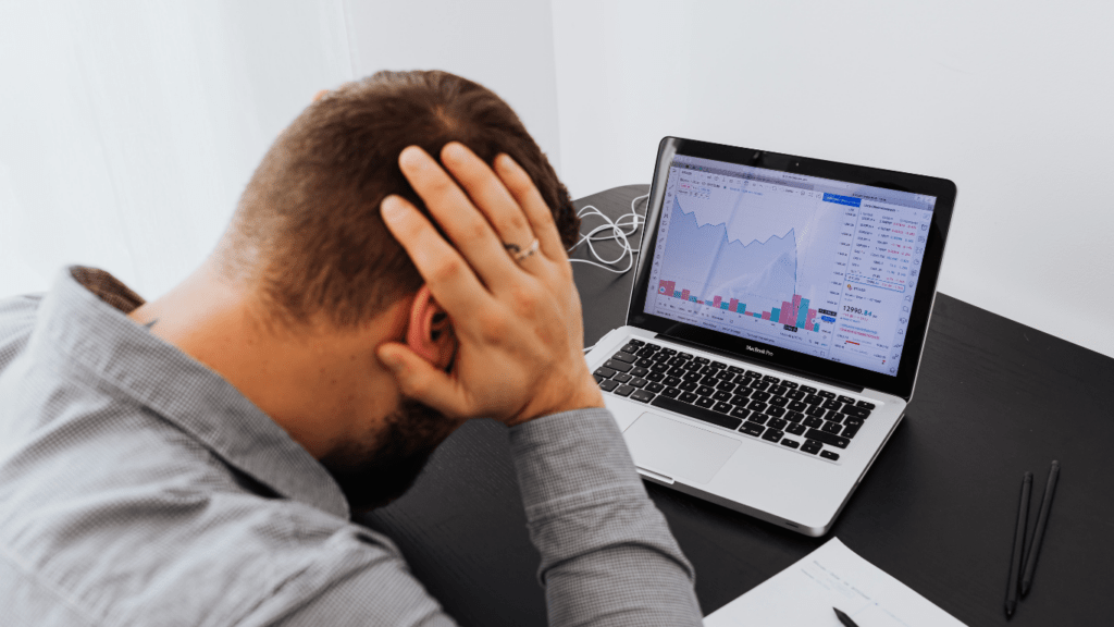 a person sitting at a desk with their head in their hands while looking at a laptop screen