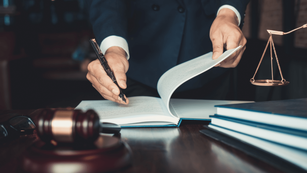 A lawyer holding a book and pen on a desk with a gavel in the background