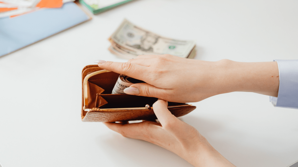 a person putting money into a wallet on a desk