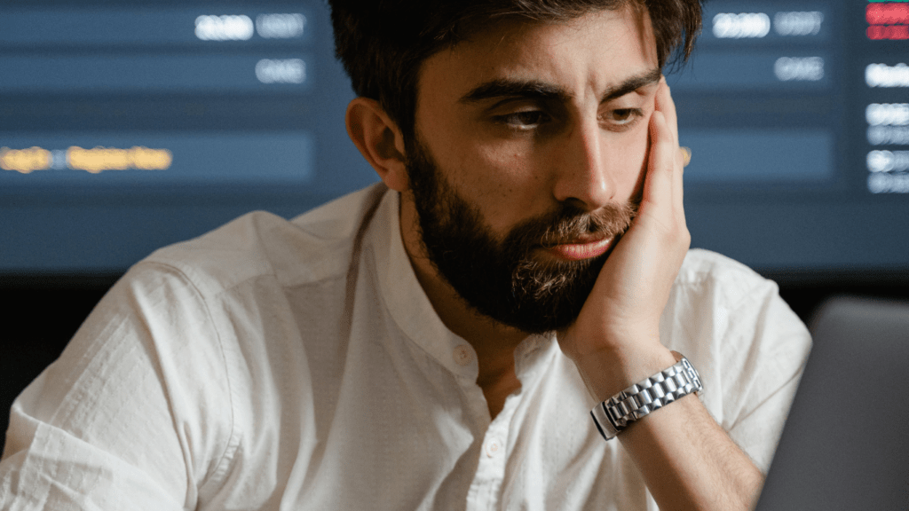 a person sitting at a desk with their head in their hands while looking at a laptop screen